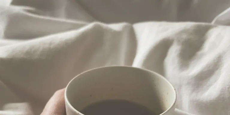 Kädet pitelevät lämmintä kuppia pehmeässä valossa