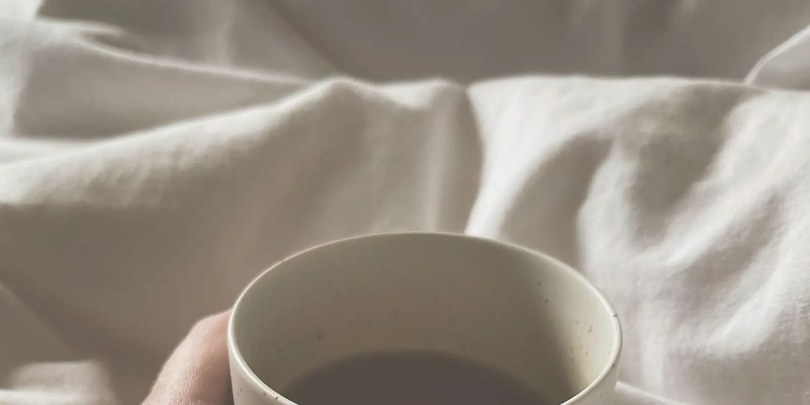 Kädet pitelevät lämmintä kuppia pehmeässä valossa