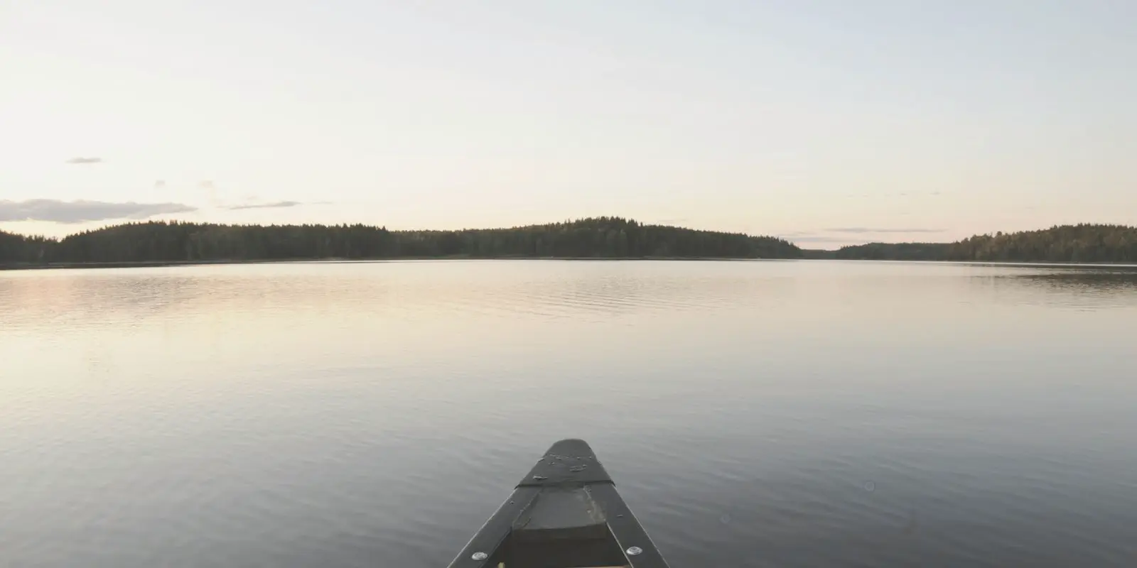 Puuvene tyynellä järvellä iltavalossa